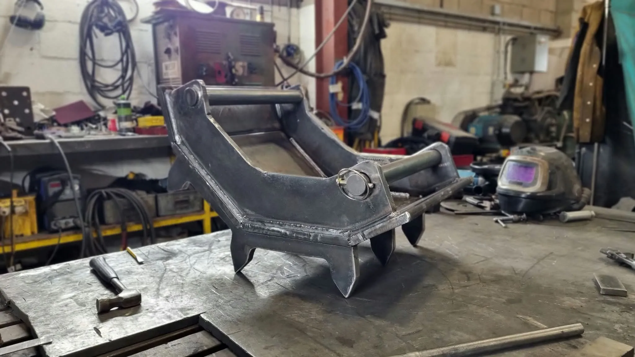 A freshly welded attachment frame on the fabrication bench at Exc@v8's Kendal workshop, mid-build