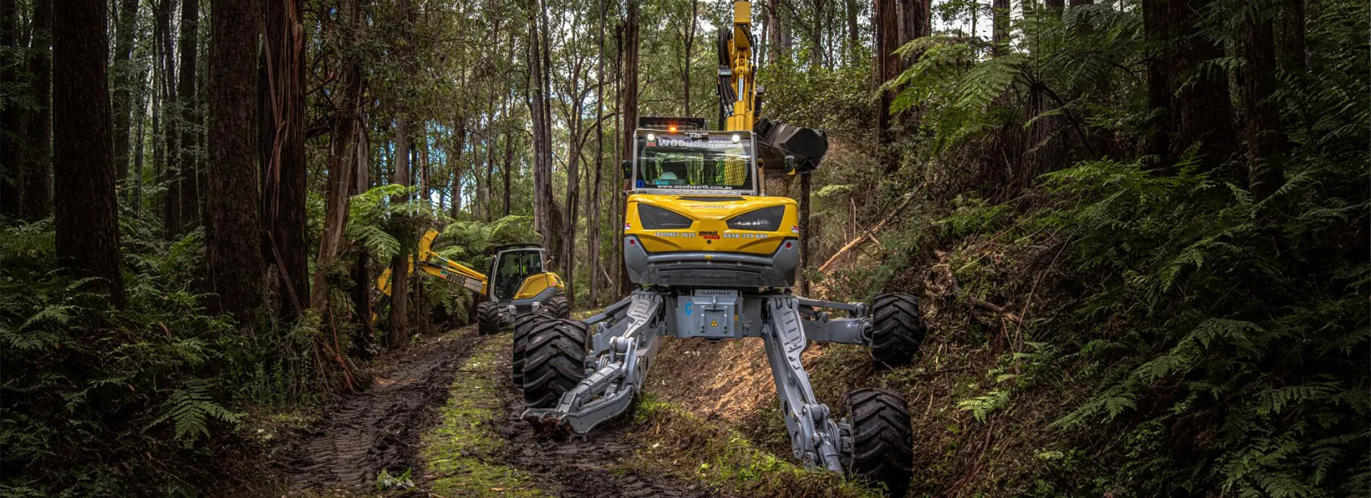 A Menzi Muck walking excavator working in a forest, its wheels set wide apart on the bank of a track