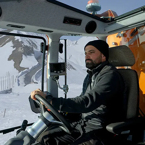 An operator in the K Trac’s cab, with wide windows onto a snowy mountain road